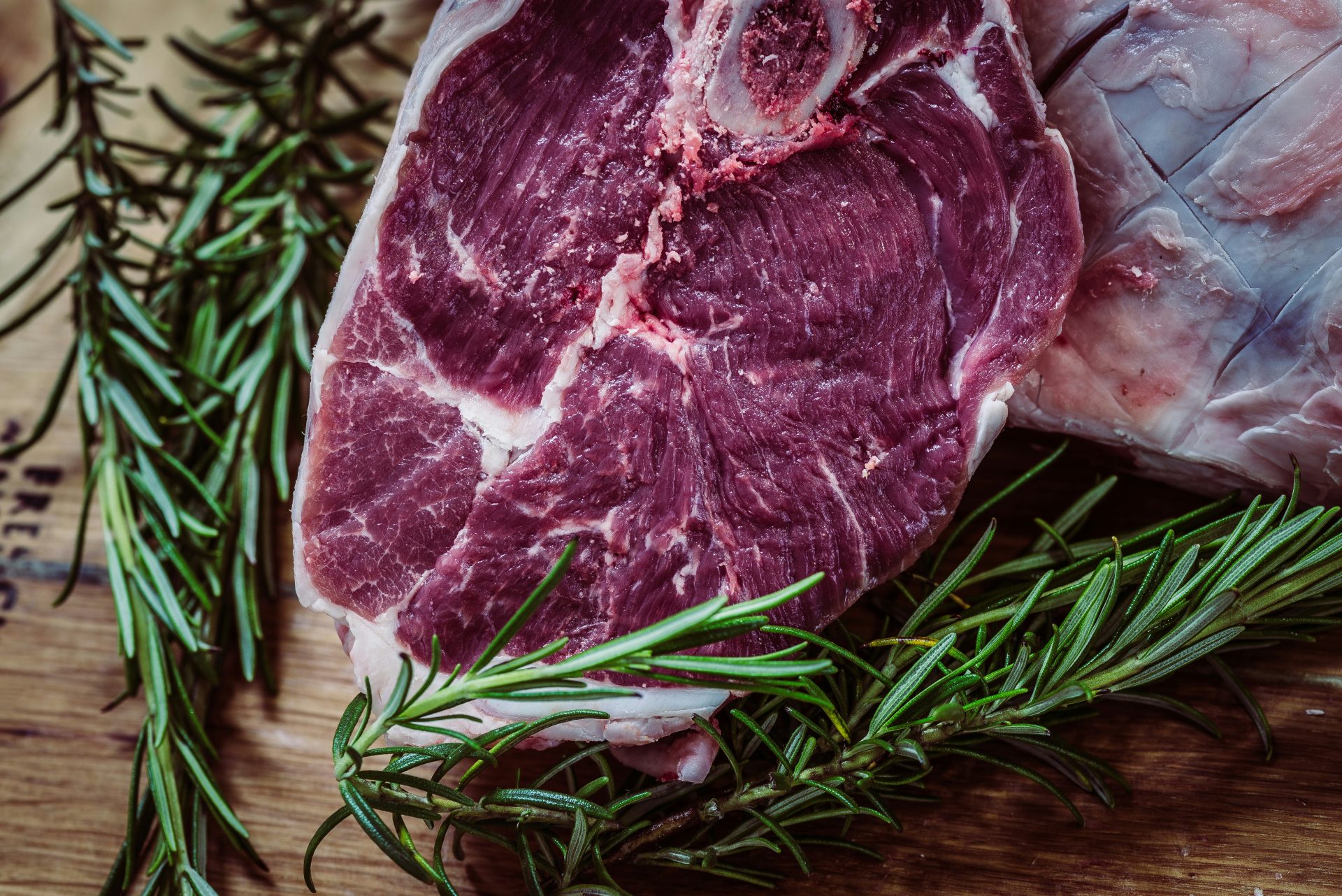 Raw lamb chop with rosemary herb garnish.